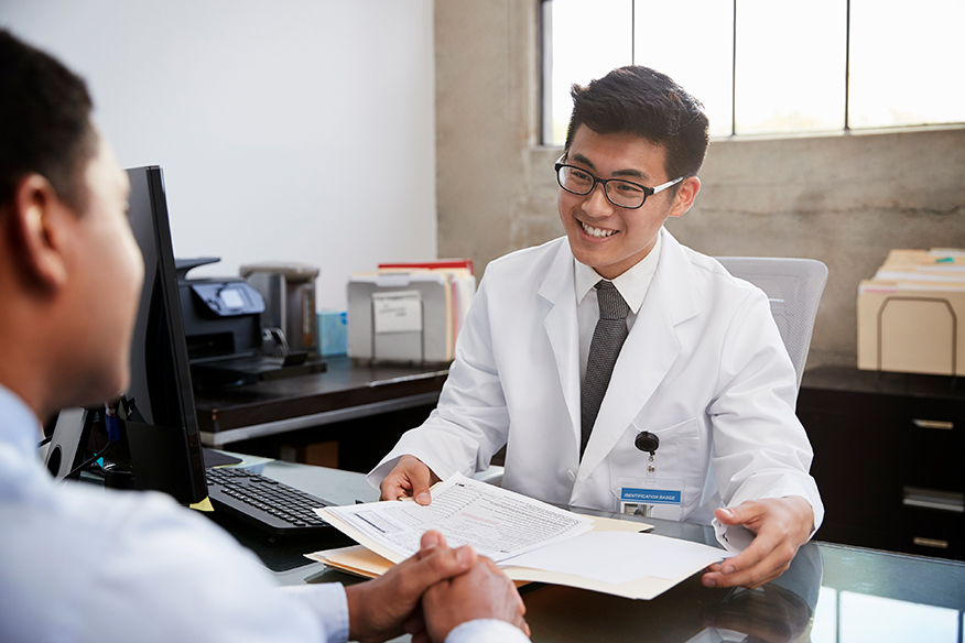 male doctor sitting behind desk speaking with patient